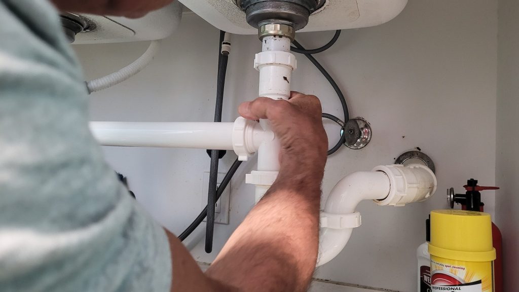 Handyman at home tightening seals on plumbing pipes to stop a leak at kitchen sink.